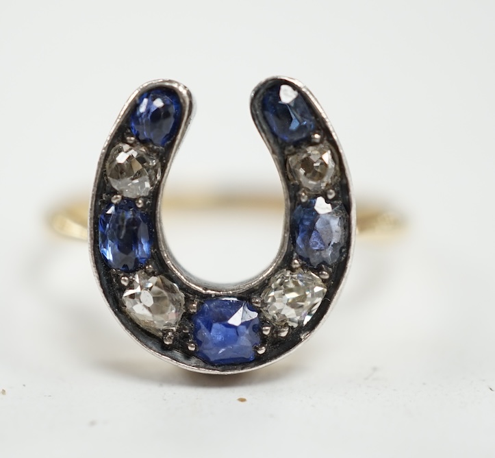 An early 20th century yellow metal (stamped 15), sapphire and diamond cluster set horseshoe shaped ring, size M, gross weight 2.8 grams. Condition - poor to fair